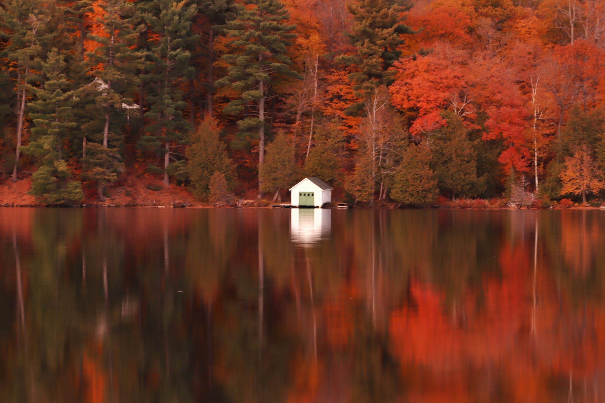 Maison blanche au bord d'un lac entouré de forêt aux couleurs d'automne, région d'Ottawa, Ontario, Canada