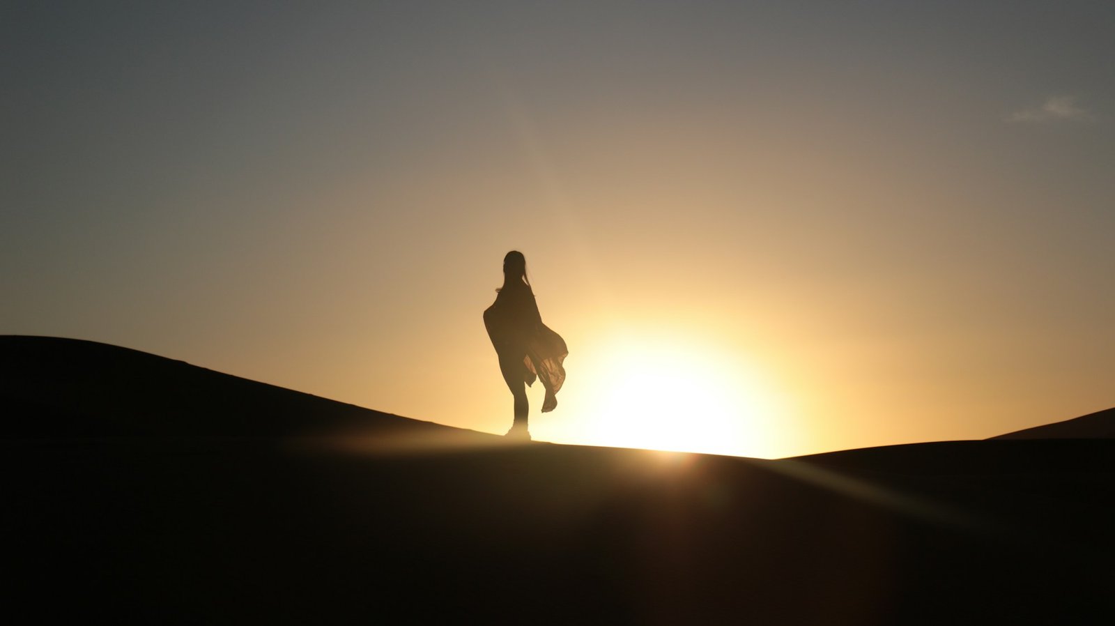 Silhouette d'un voyageur marchant sur une dune de sable dans le désert du Sahara au coucher du soleil