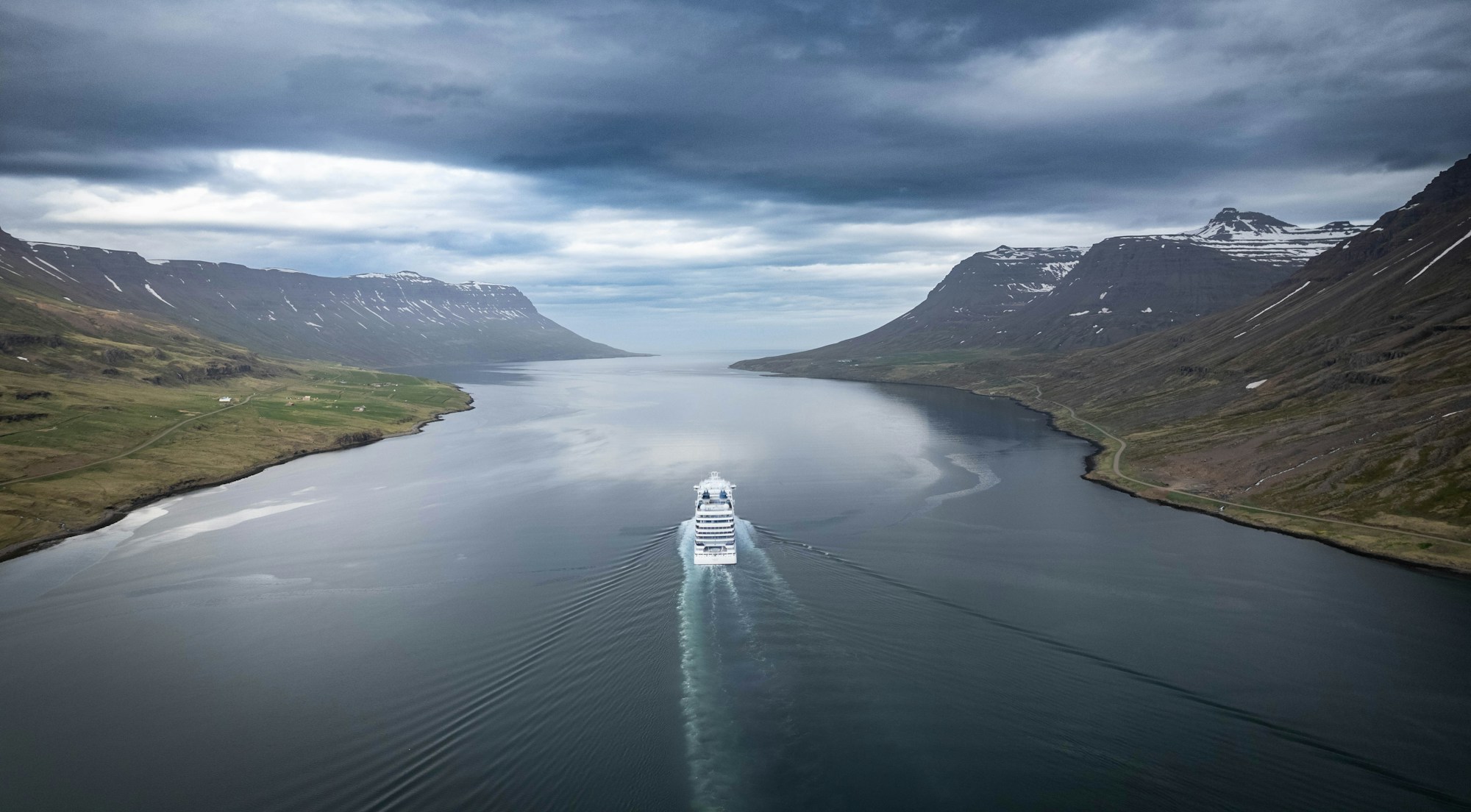Cruise ship sailing through a fjord surrounded by snow-capped mountains