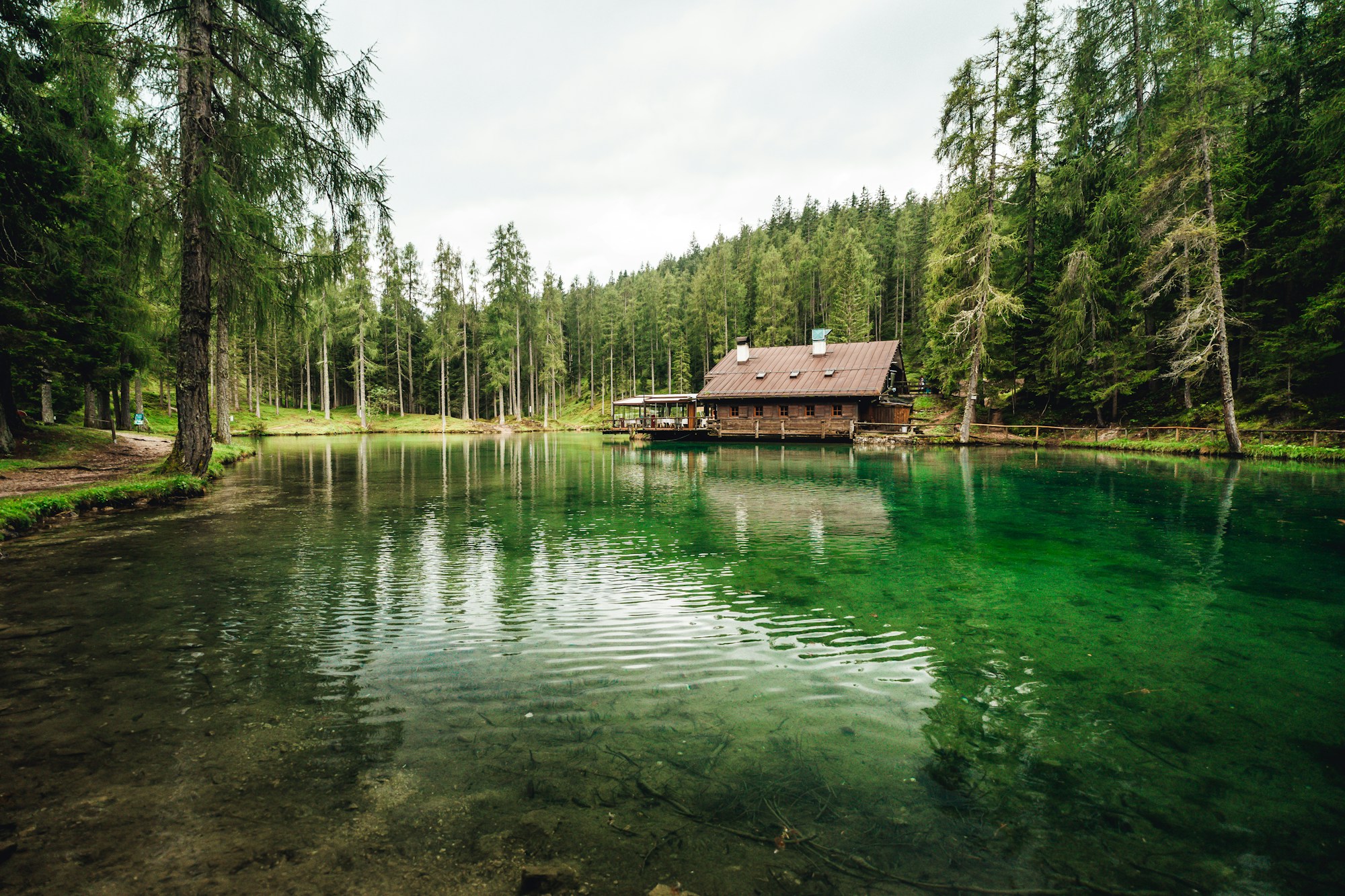 Wooden cabin on a crystal-clear lake surrounded by alpine forest, reflections in the water