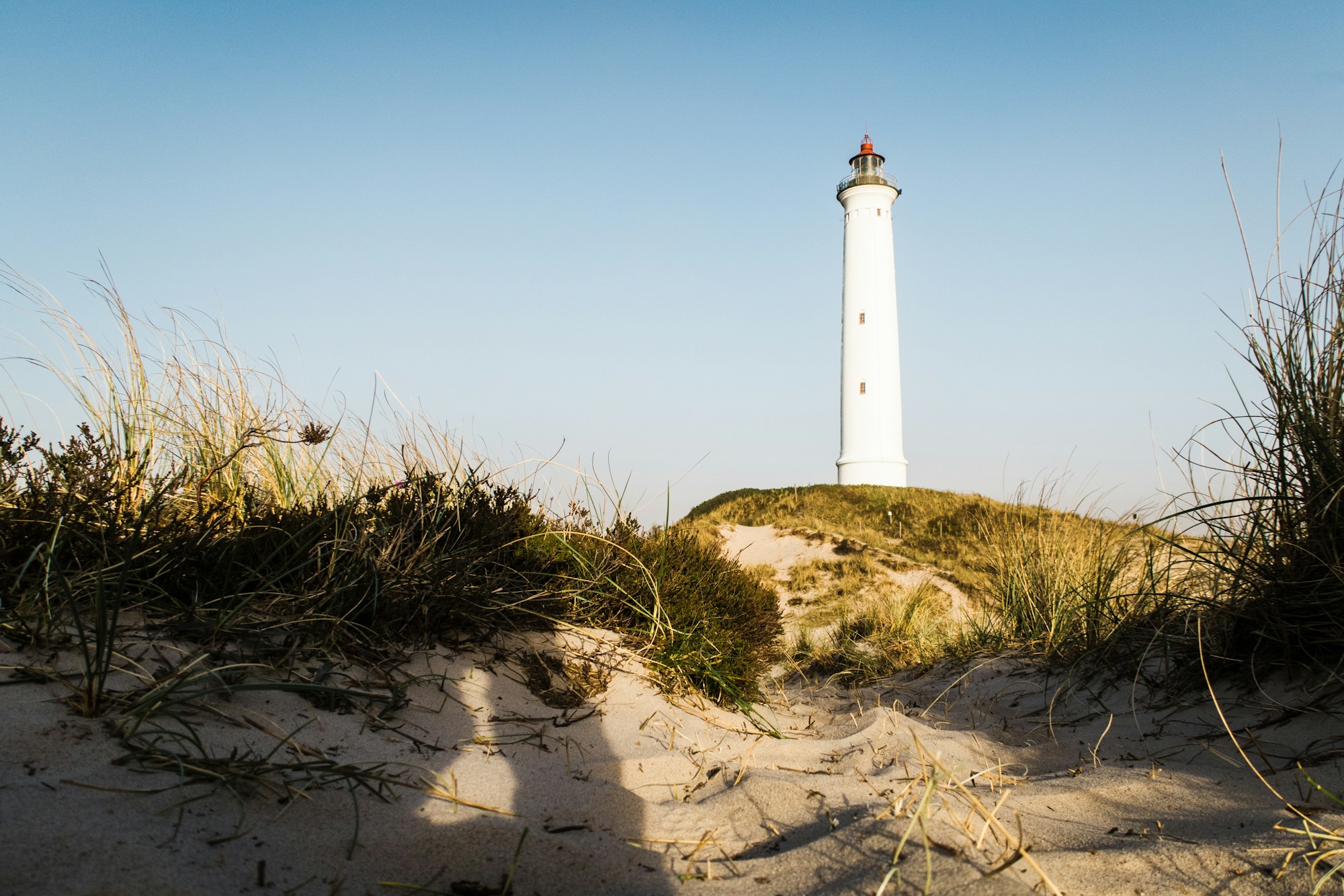 White lighthouse under a blue sky by the sea, Danish or Nordic coast