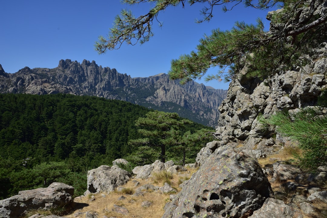 Sentier rocheux du GR20 en Corse avec vue sur les aiguilles de Bavella et le maquis méditerranéen