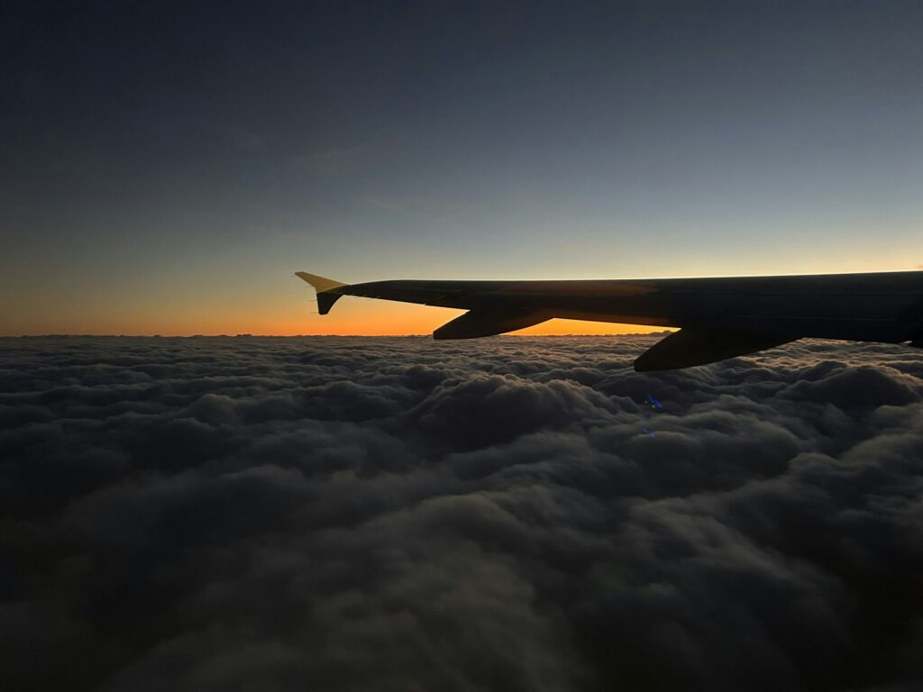 Aile d'avion au-dessus des nuages au coucher du soleil, illustrant le voyage long-courrier et le décalage horaire