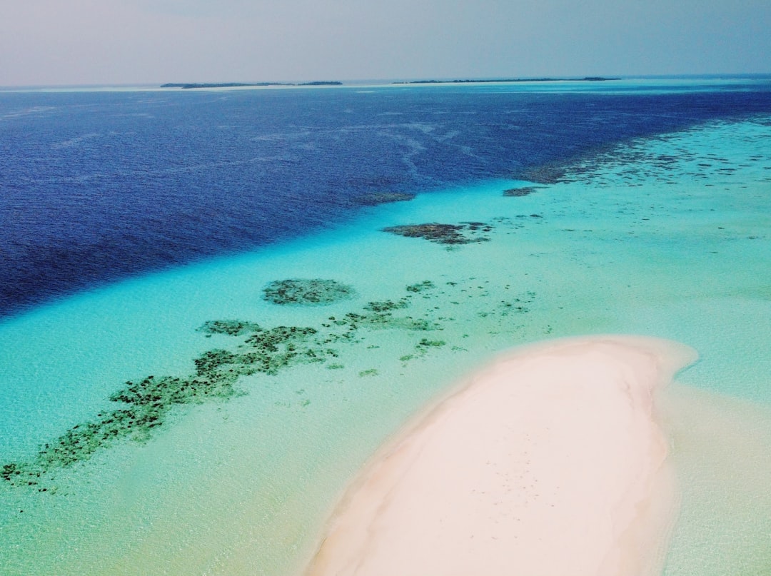Aerial view of an isolated Maldivian beach with shallow emerald-colored lagoon