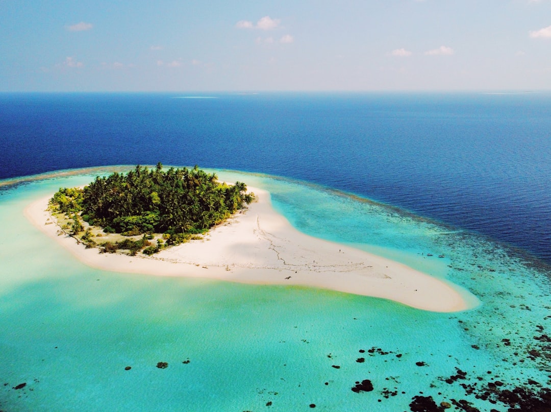 Aerial view of an isolated Maldivian island surrounded by a lagoon in shades of blue