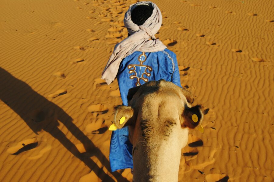 Guide berbère en robe bleue menant un dromadaire dans le désert du Sahara