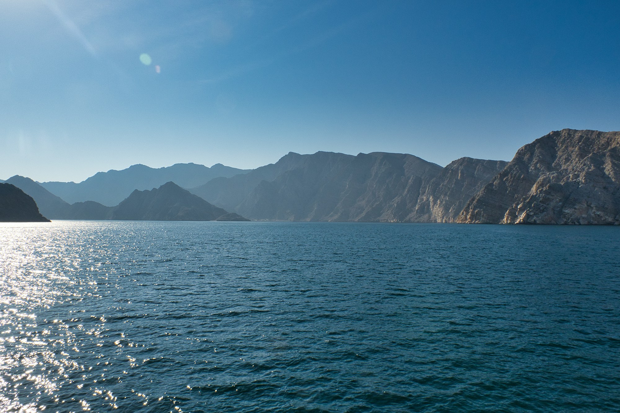 Mer bleue calme et montagnes rocheuses de Salalah, Oman, coucher de soleil doré