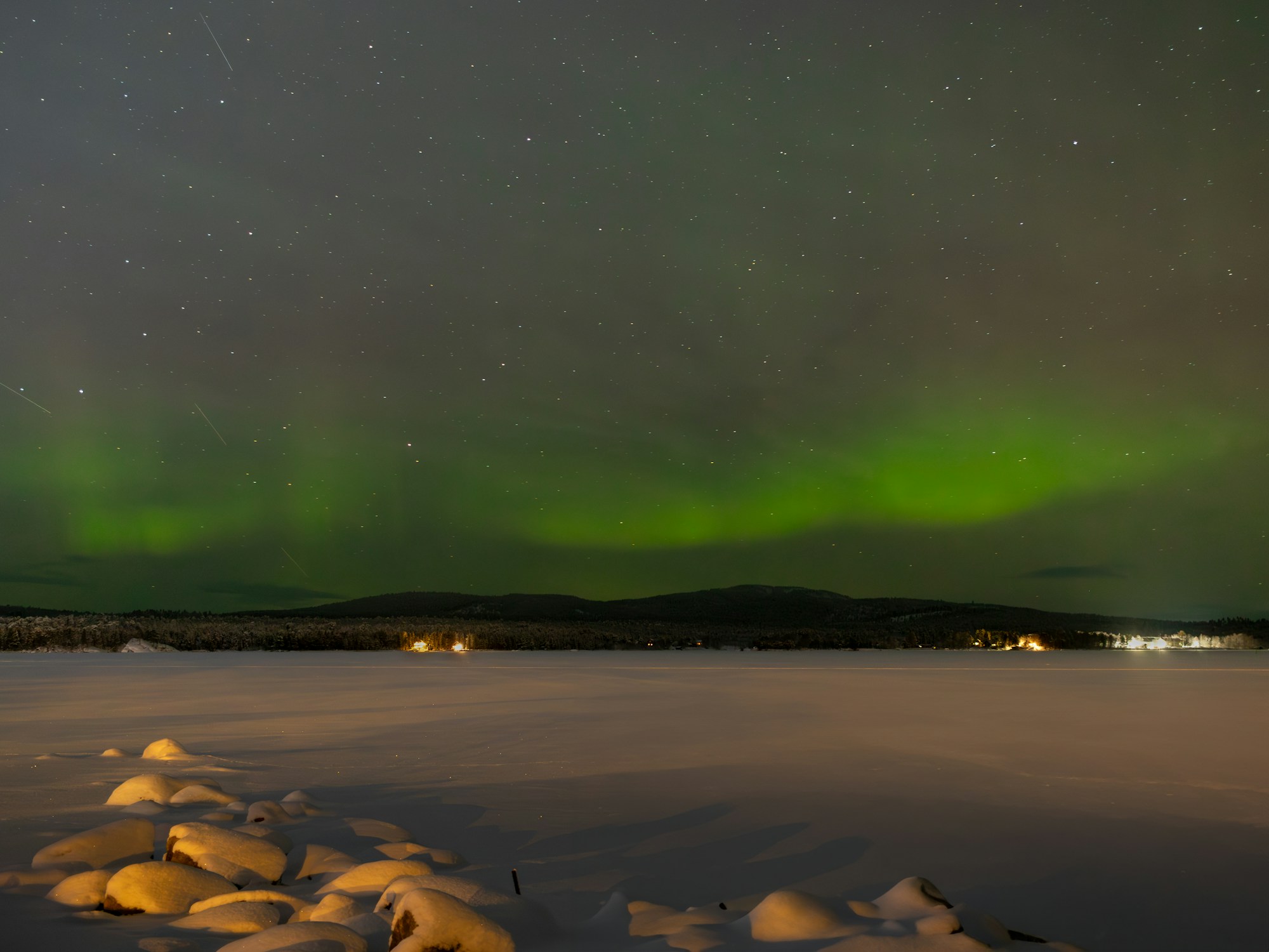 Aurores boréales bleues et vertes se reflétant sur le lac Inari gelé en Finlande, entouré de forêts de pins enneigés