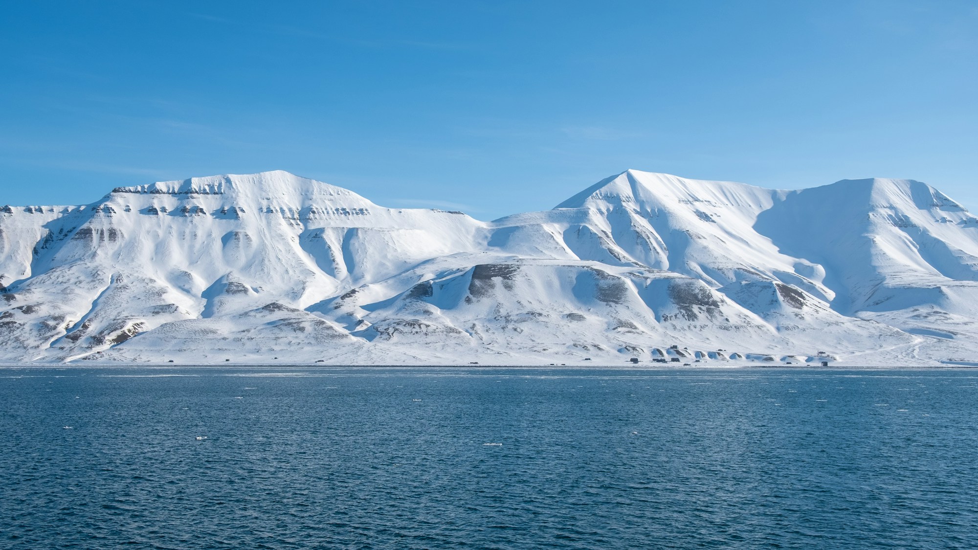 Montagnes enneigées aux sommets acérés dominant une mer bleue glaciale à Svalbard, archipel arctique norvégien