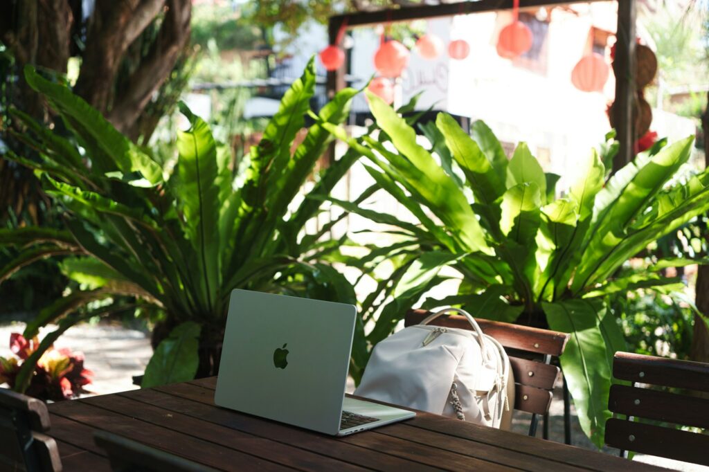 Ordinateur portable et sac à dos sur une table en bois entourée de plantes — digital nomad lifestyle