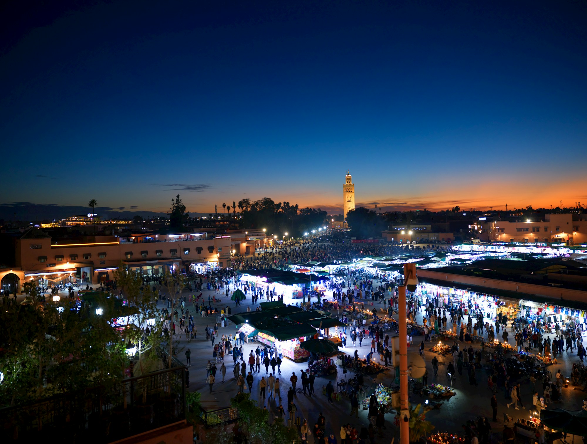 La place Djemaa el-Fna de Marrakech au crépuscule, stands lumineux et foule animée