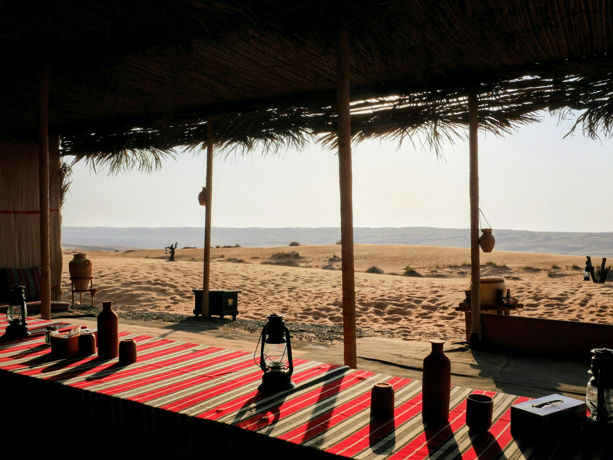 Camp désertique traditionnel en Oman avec tapis rouges et dunes dorées en arrière-plan