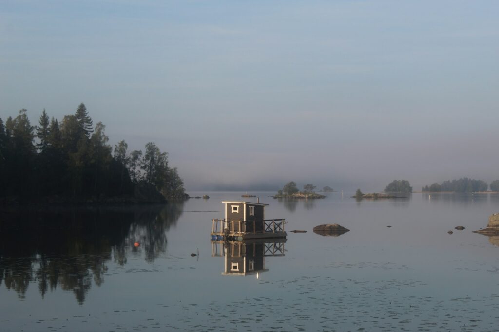 Sauna en bois flottant sur un lac finlandais au coucher du soleil, symbole de la tradition du bain communautaire scandinave