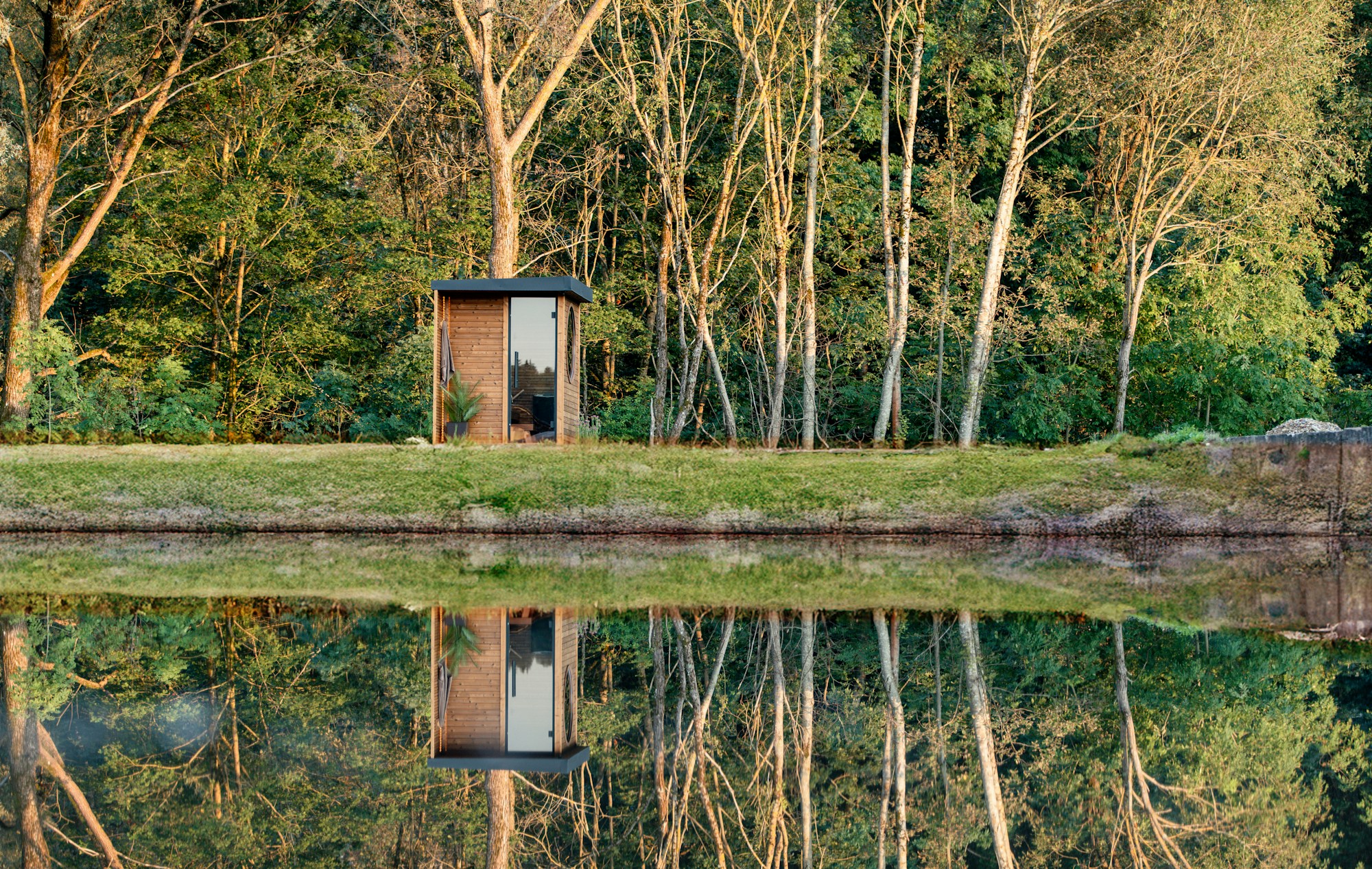 Small wooden sauna cabin with round windows, nestled in a Nordic forest by a calm lake