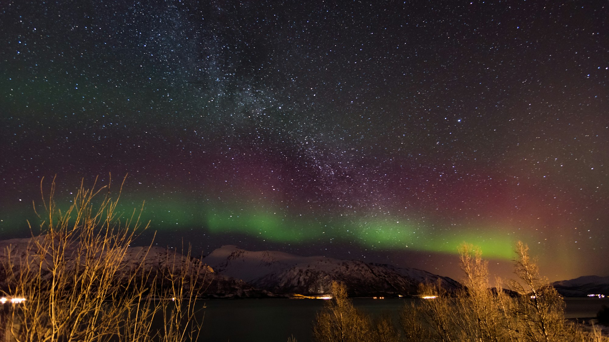 The Northern Lights dance in the sky over Tromsø, Norway, creating a green light show over the snow