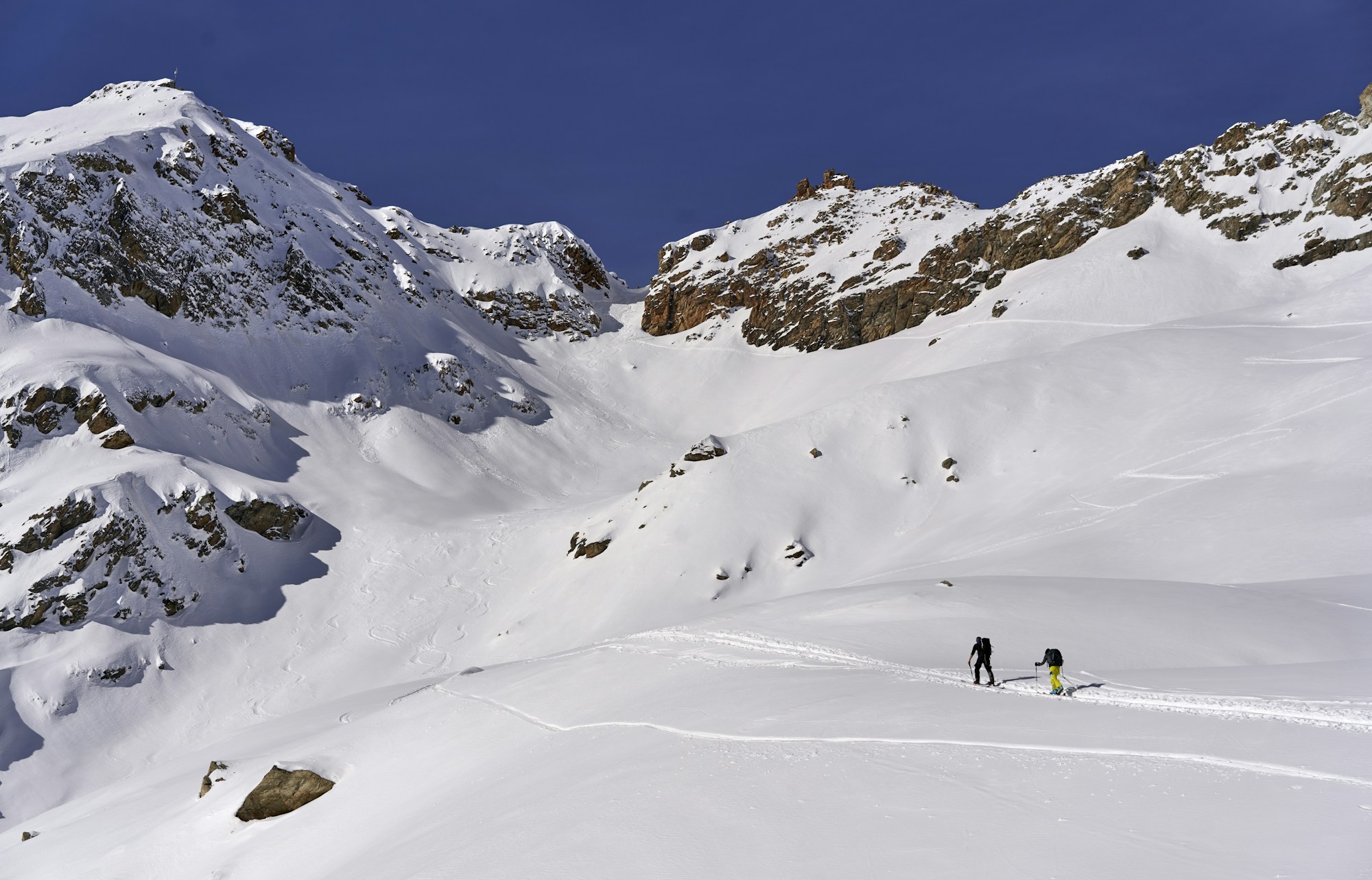 Skieur de randonnée remontant vers un col enneigé dans les Alpes suisses