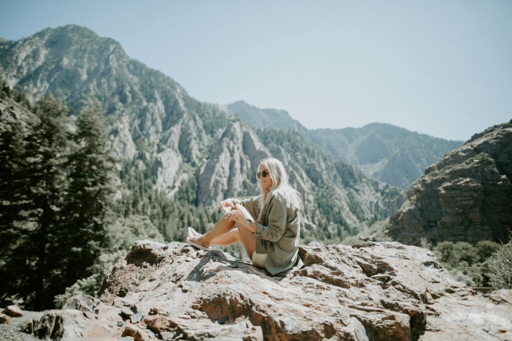 Femme voyageant seule, assise sur un promontoire rocheux face aux montagnes, contemplant la nature — solo dating travel 2026