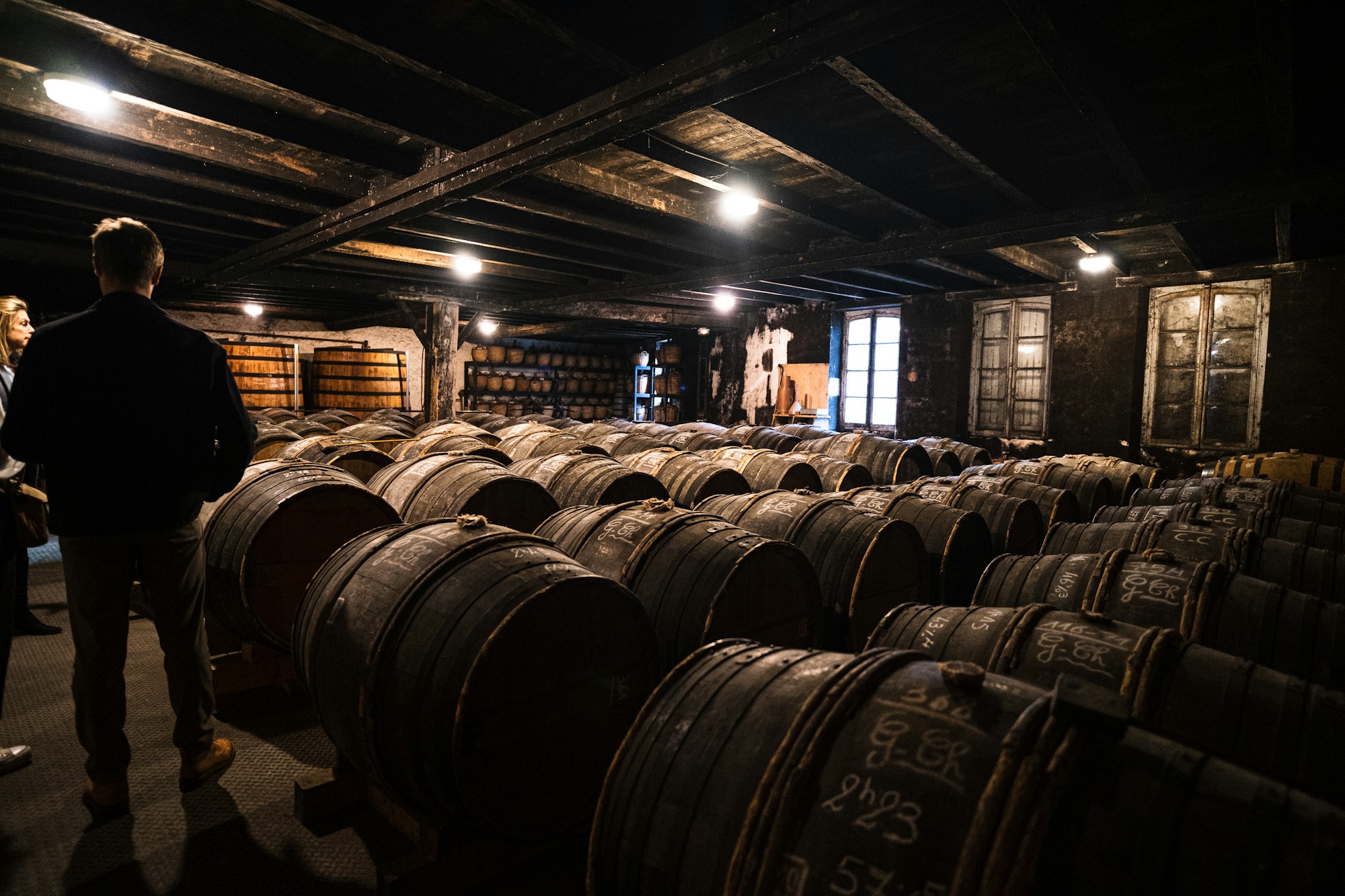 Man standing before rows of cognac barrels in the darkened Delamain cellar, Jarnac, France