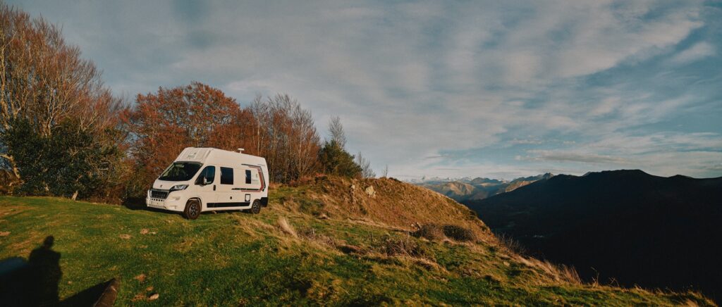 Van aménagé garé sur une colline verdoyante avec des montagnes en arrière-plan