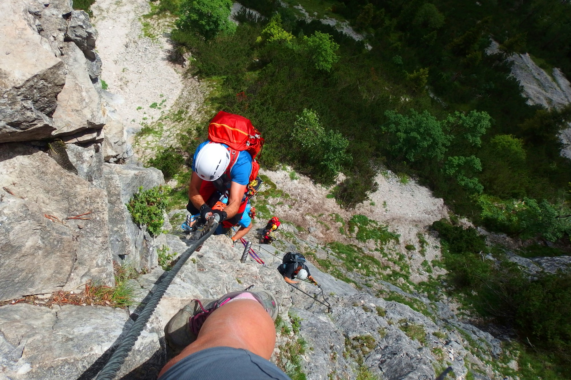 Grimpeur sur une via ferrata dans les Alpes suisses avec câbles et marches métalliques face à une paroi rocheuse