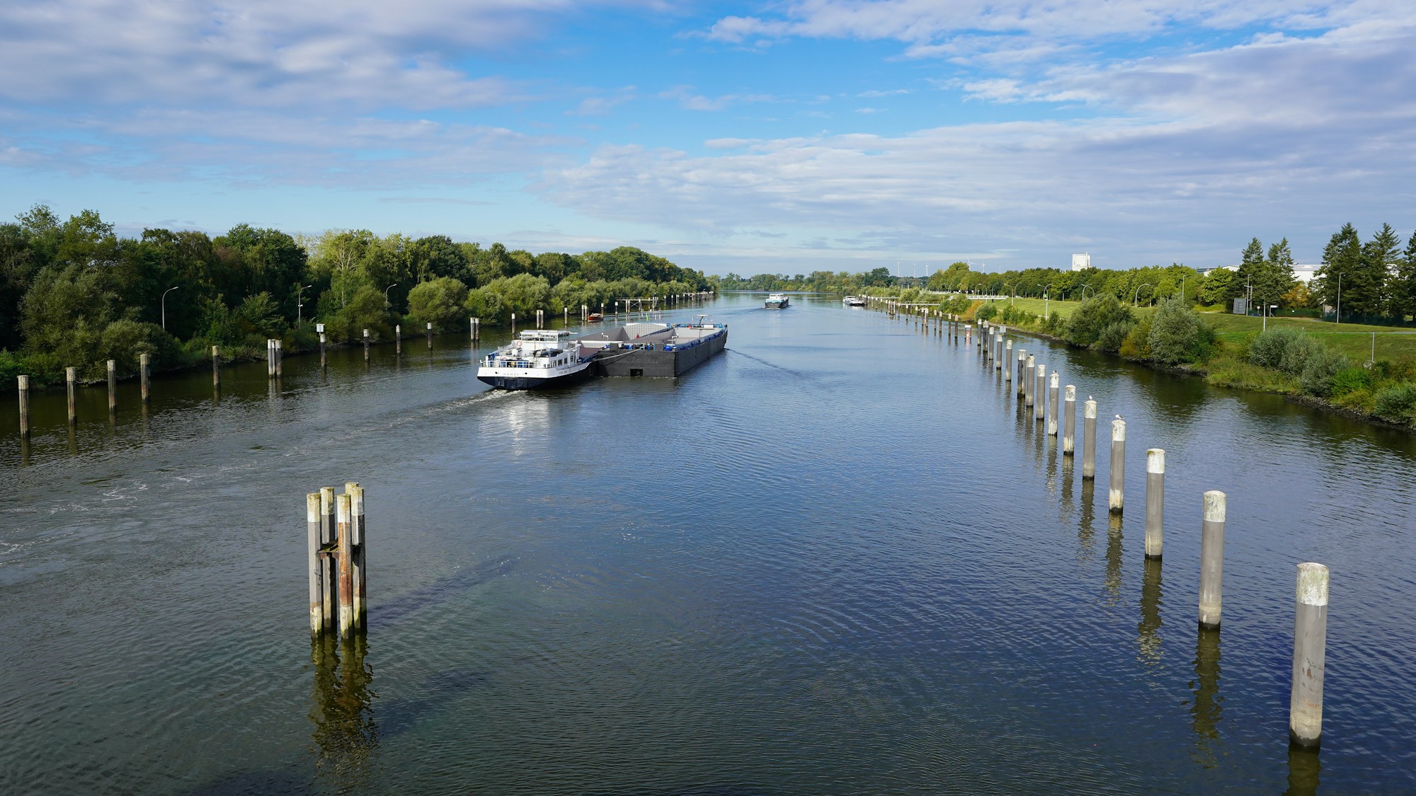 Barge cruising peacefully along a wide tree-lined canal in Europe