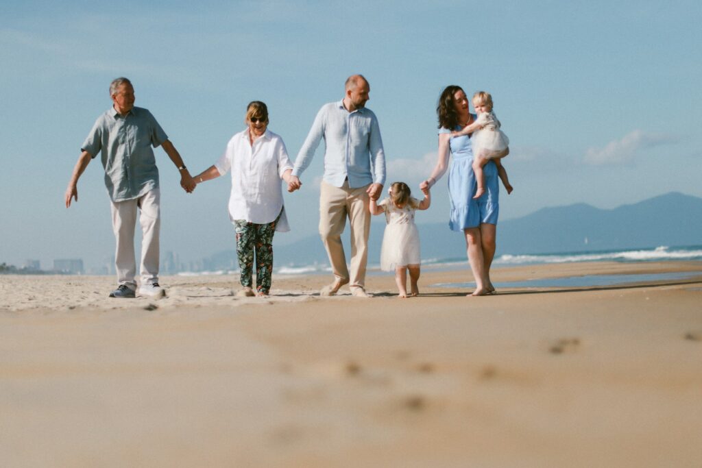 Famille multigénérationnelle marchant ensemble sur une plage de sable — voyage skip-gen 2026