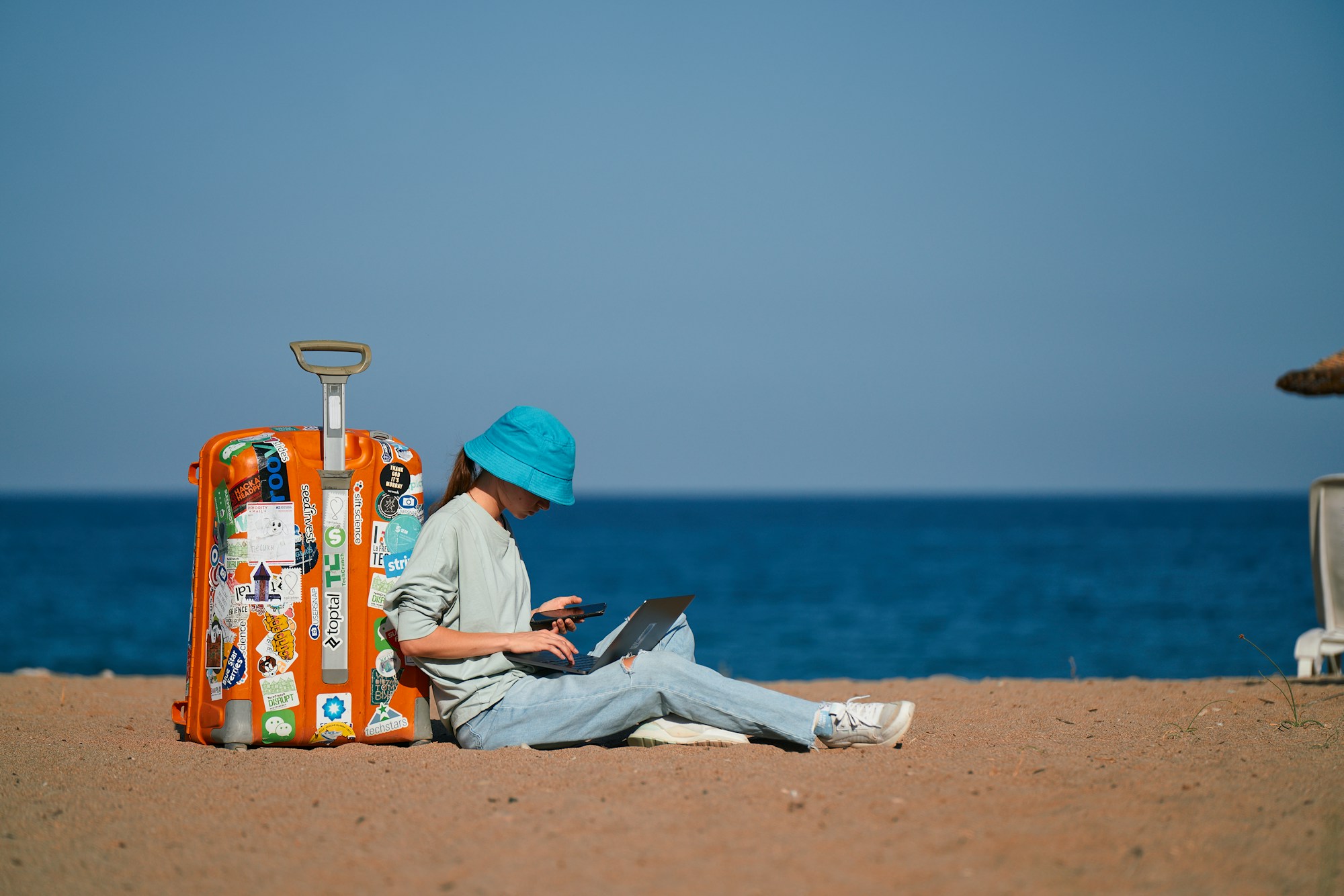 Voyageuse planifiant ses vacances Black Friday sur un ordinateur portable en bord de mer au coucher de soleil