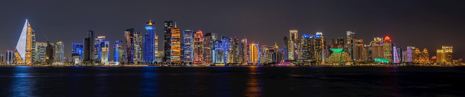 Skyline de Doha de noche con rascacielos iluminados a lo largo del paseo de la Corniche