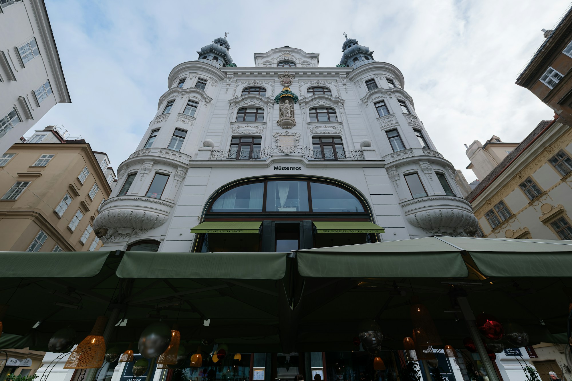 Fassade eines schönen weißen Gebäudes mit Balkonen und grünen Markisen im Wiener Rudolfsheim-Viertel, typisch für Wiener Boutiquehotels