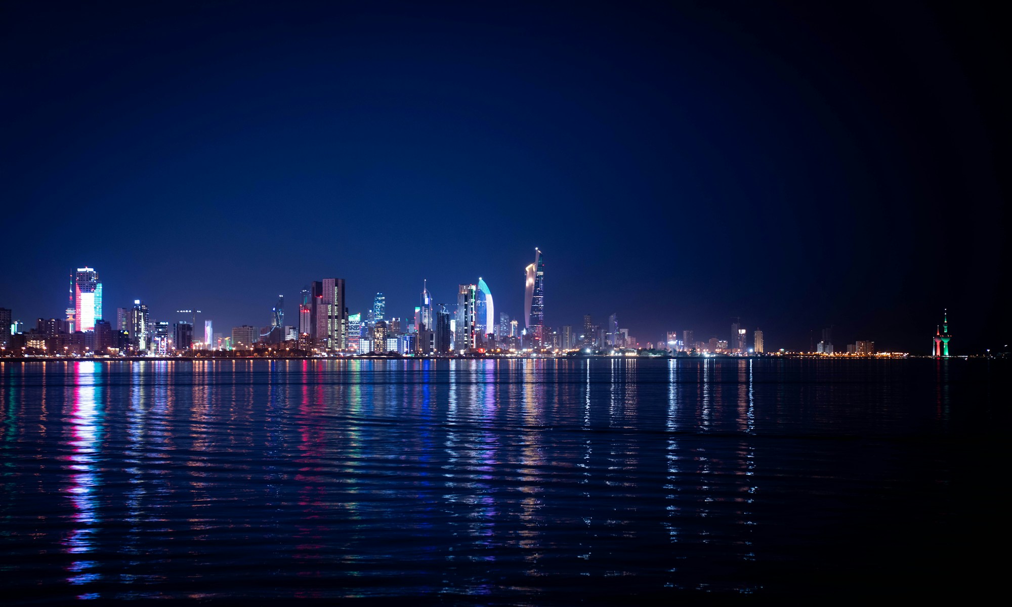 Skyline de Koweït City illuminée la nuit — reflets sur l'eau du Golfe Persique