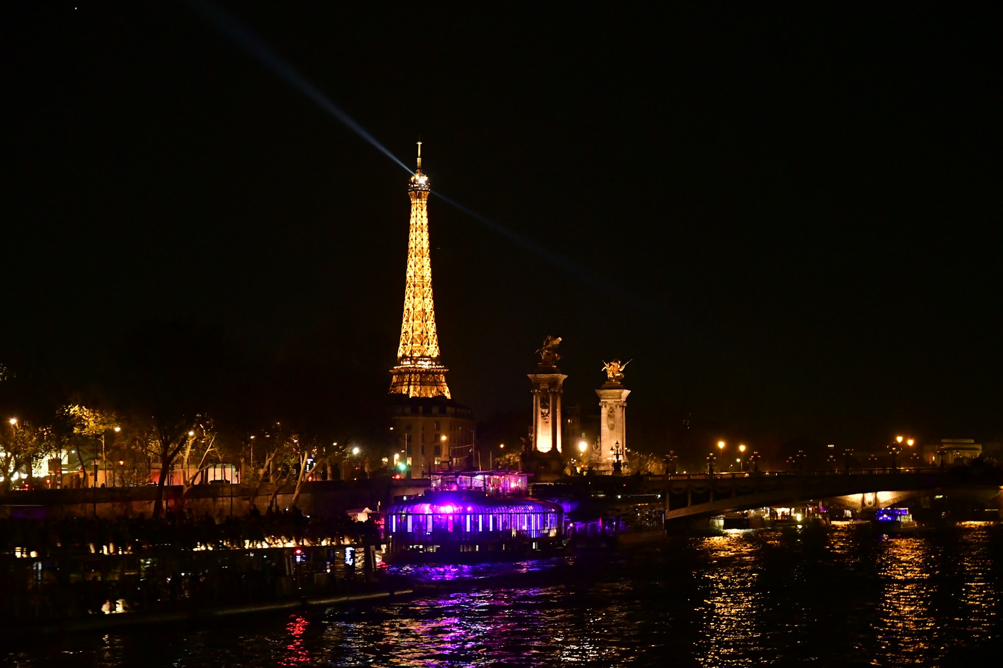 La Tour Eiffel illuminée de nuit avec un faisceau lumineux — vue depuis les quais de Paris