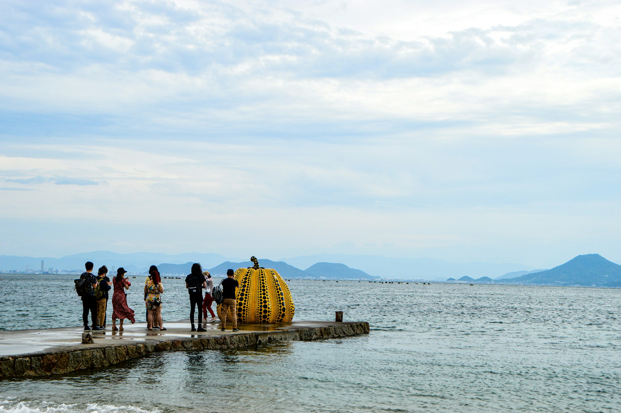 Visitors photographing Yayoi Kusama's famous yellow polka-dot pumpkin on Naoshima island, Japan