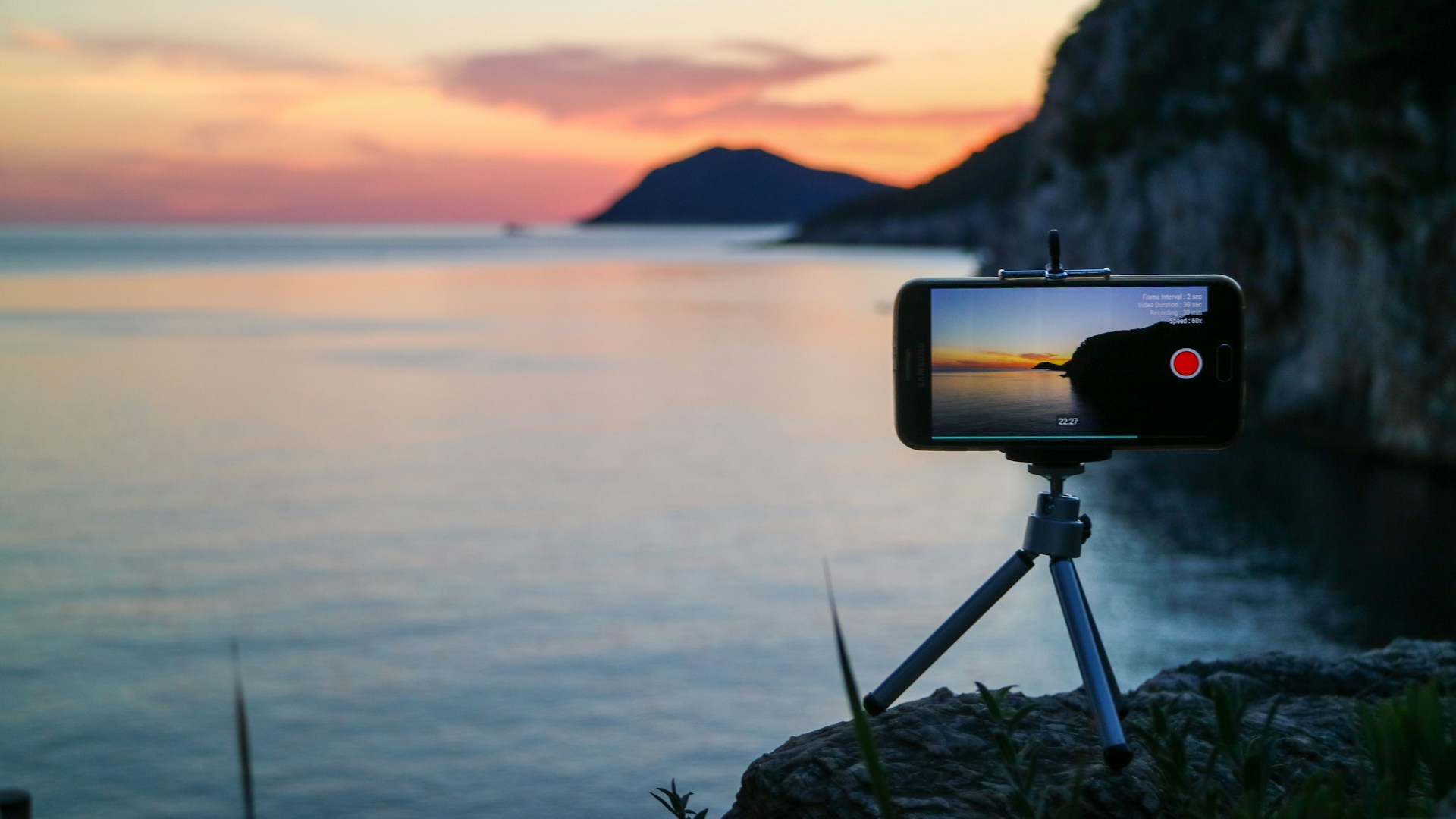 Créateur filmant un coucher de soleil depuis un promontoire, symbolisant le travail des vidéastes voyage