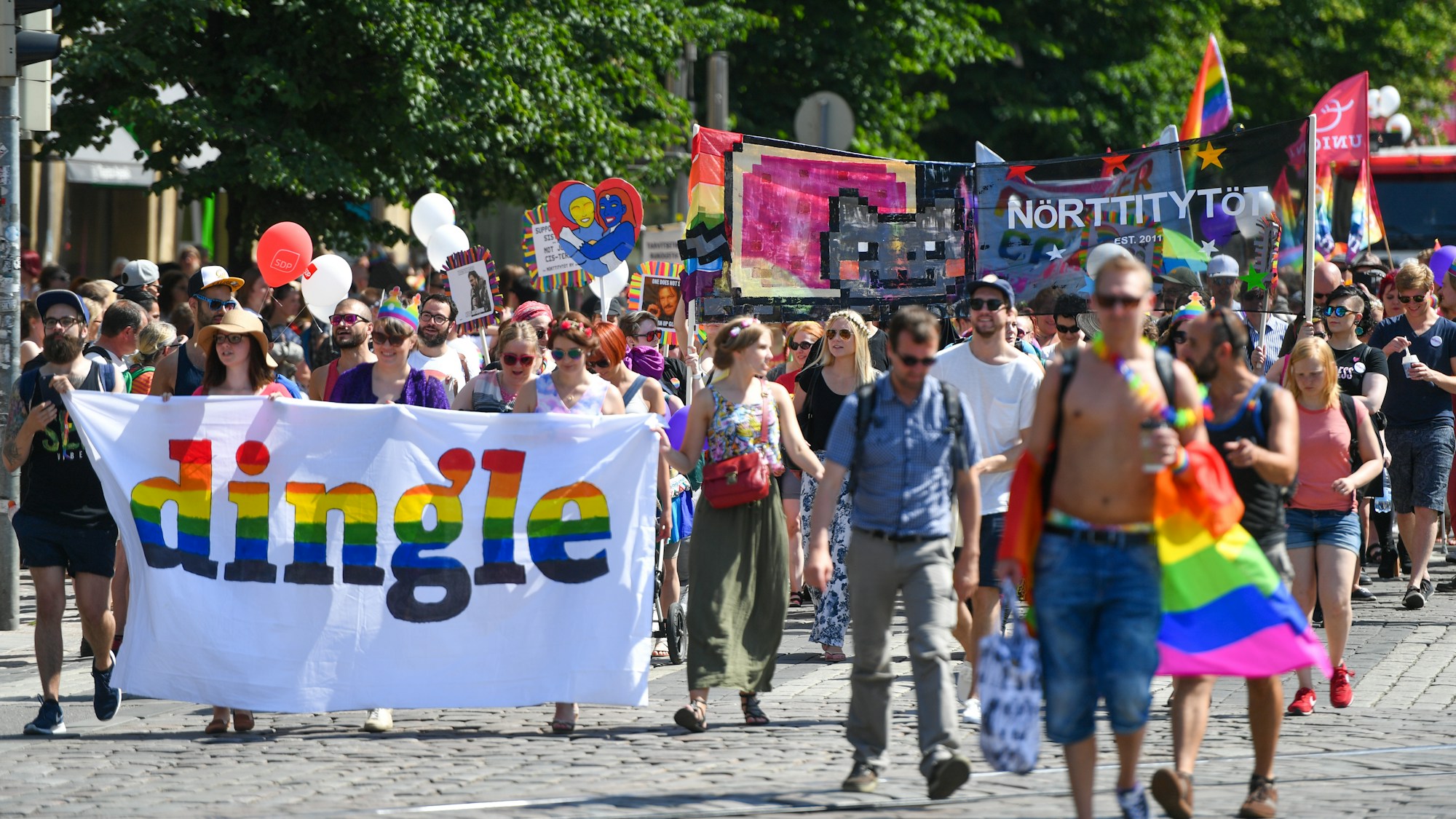 Parade de la Gay Pride dans une avenue animée avec drapeaux arc-en-ciel et foule festive