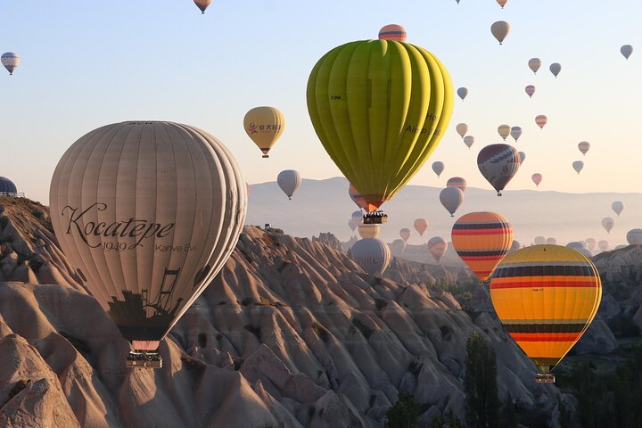 Vol en montgolfière au lever du soleil au-dessus des cheminées de fée de Cappadoce, paniers colorés dans le ciel rosé