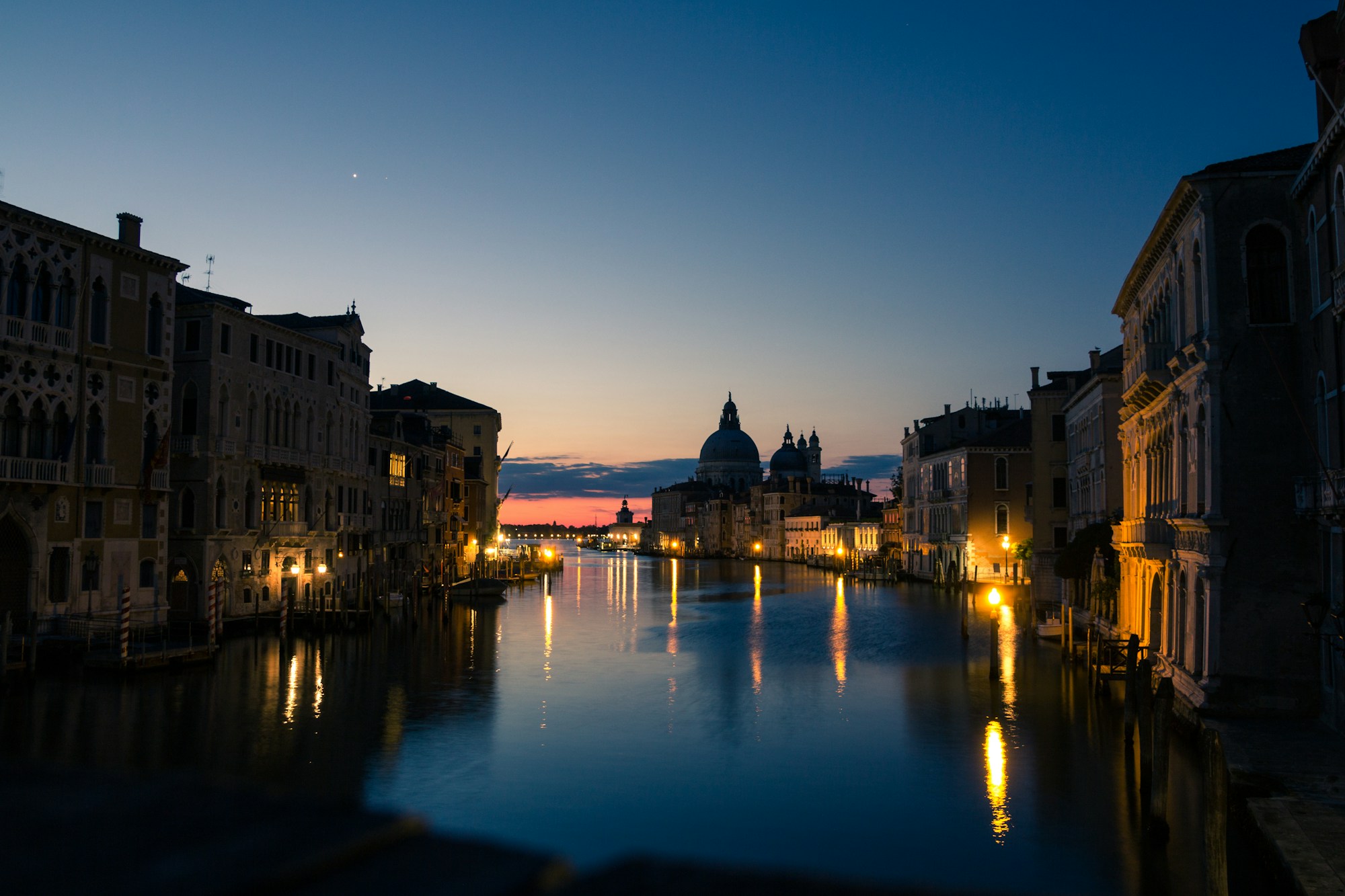 Venice canal at night with reflections of illuminated palazzi on the dark water