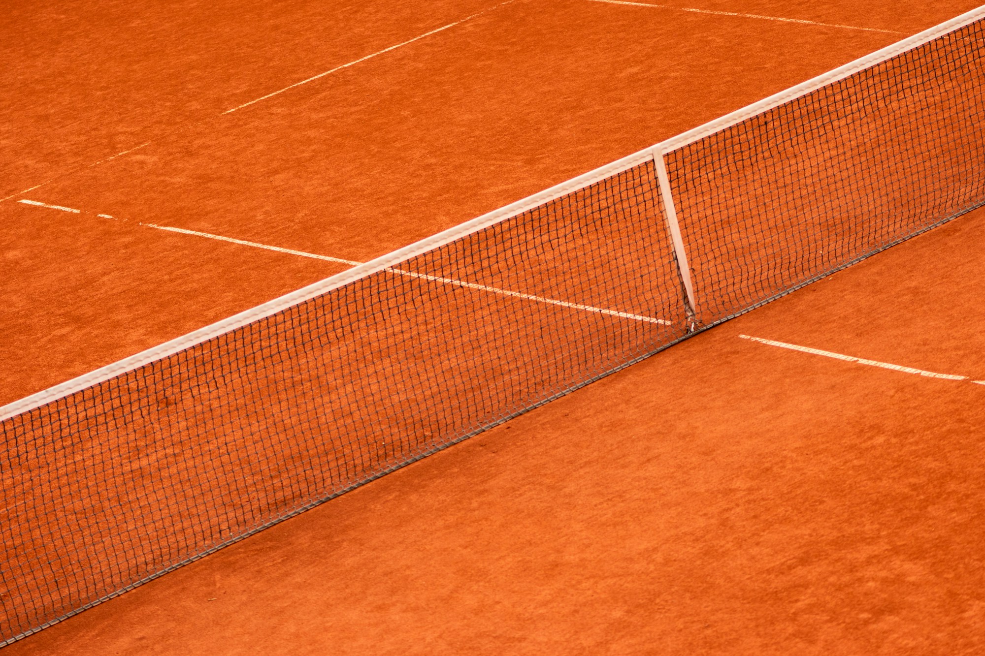 Red clay tennis court during an outdoor ATP tournament, balls and net in the foreground