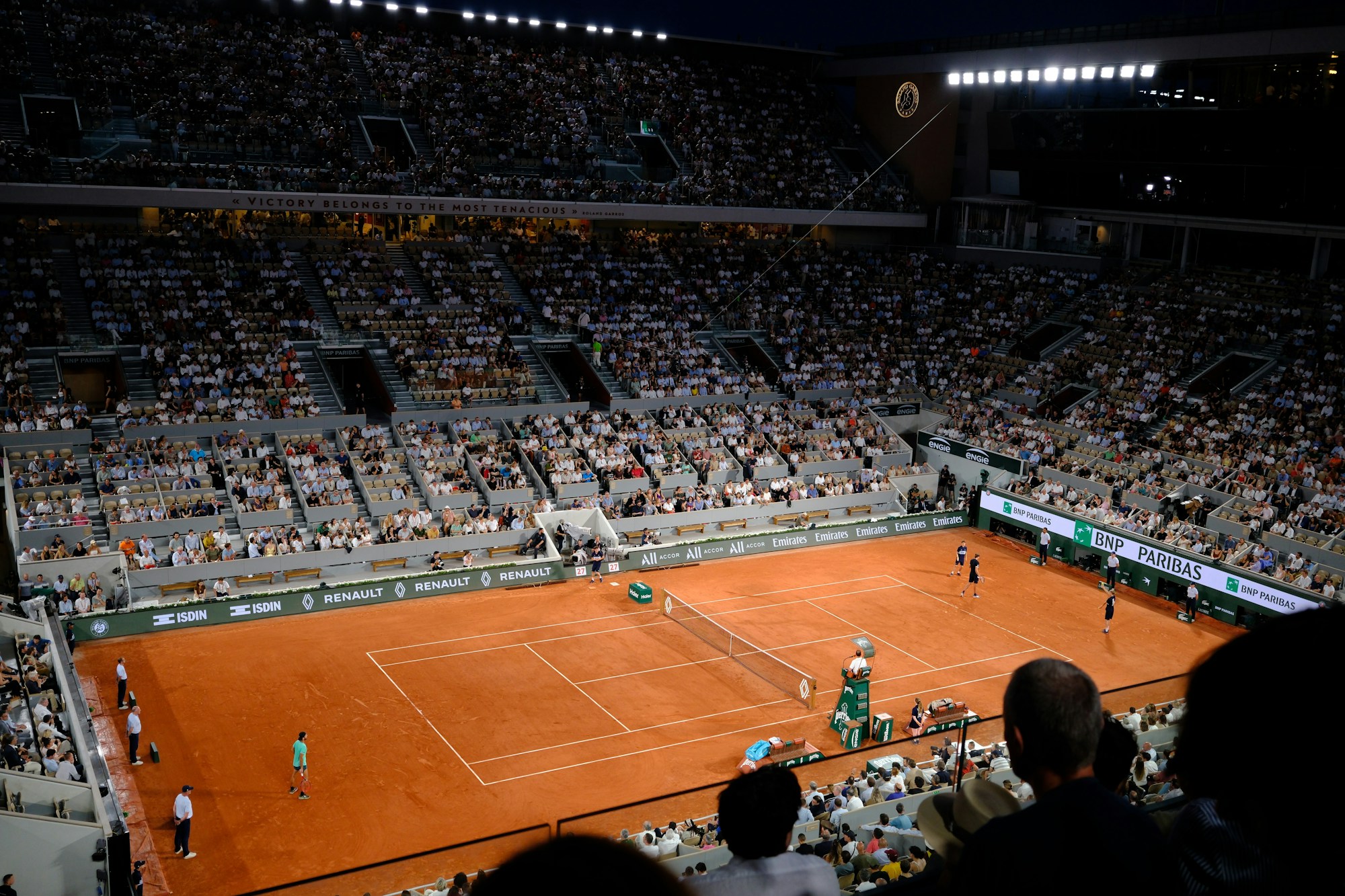 Full grandstand during a clay-court tennis match, outdoor summer atmosphere
