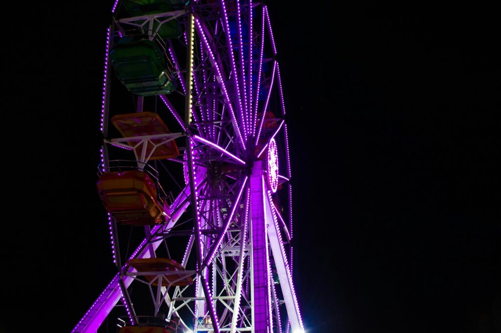 Grande roue illuminée de fête foraine nocturne, ambiance de feria populaire