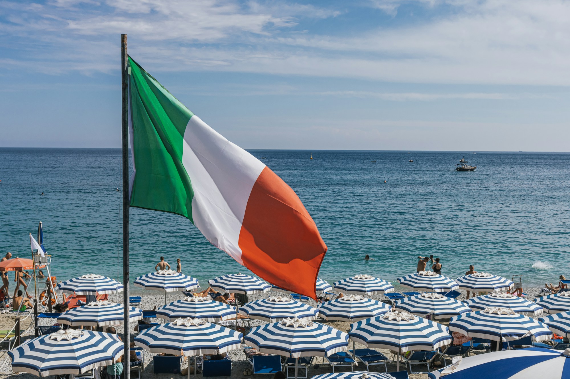 Playa italiana llena de sombrillas de colores bajo una gran bandera, ambiente de la Riviera romañola