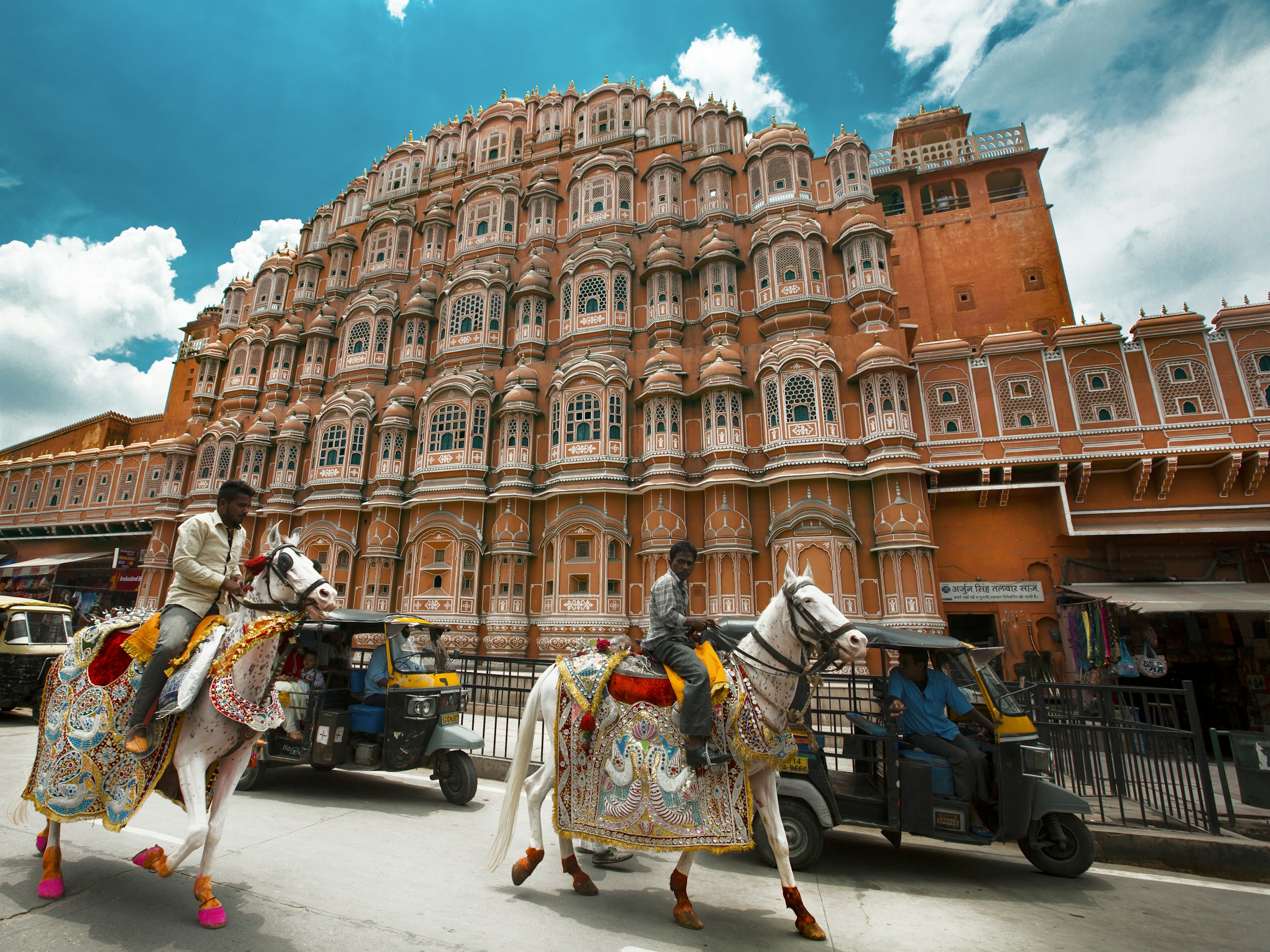 Due uomini a cavallo su cavalli bianchi decorati davanti all'Hawa Mahal di Jaipur