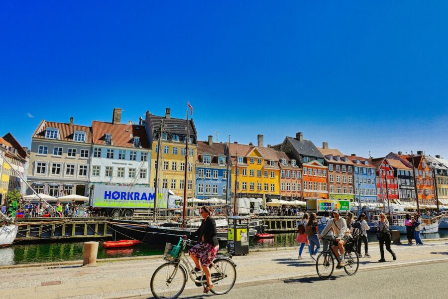 Façades colorées le long d'un canal de Copenhague, avec des cyclistes qui passent sur le quai