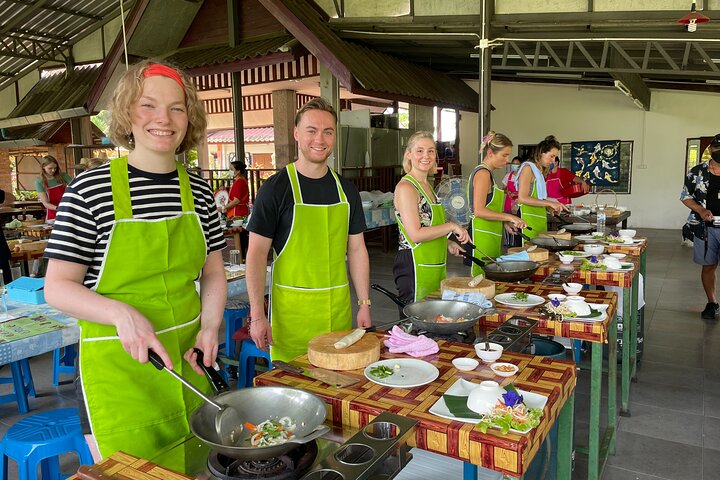 Cuisiniers en tablier vert devant leurs woks pendant un cours de cuisine thaïlandaise