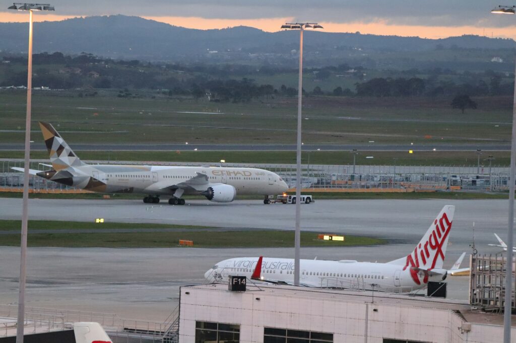 Avions de ligne, dont un Etihad et un Virgin Australia, sur le tarmac d'un aéroport australien au crépuscule