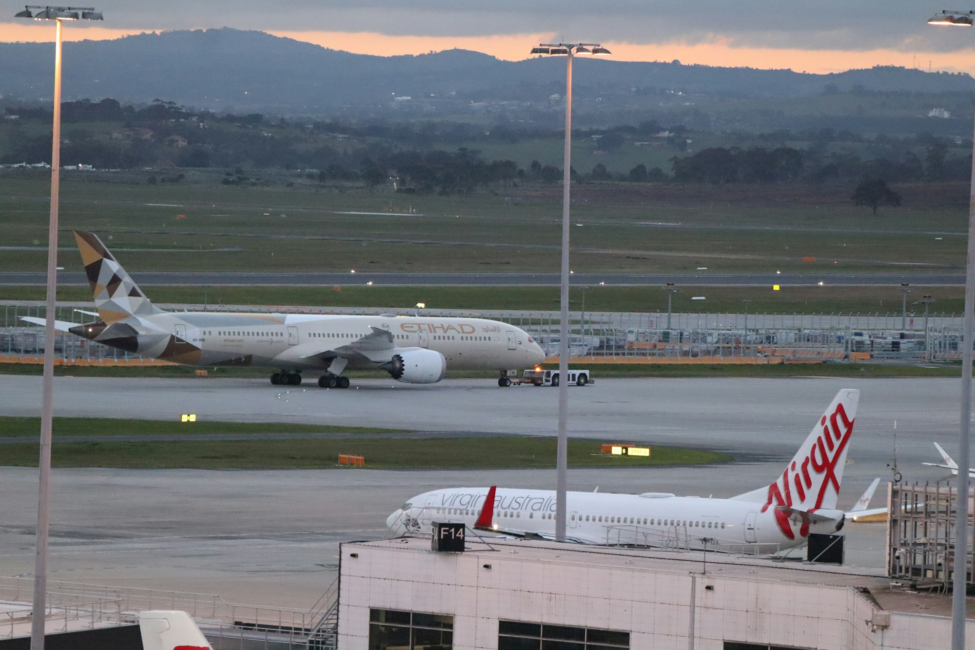 Flugzeuge, darunter ein Etihad- und ein Virgin-Australia-Flugzeug, auf dem Vorfeld eines australischen Flughafens in der Abenddämmerung