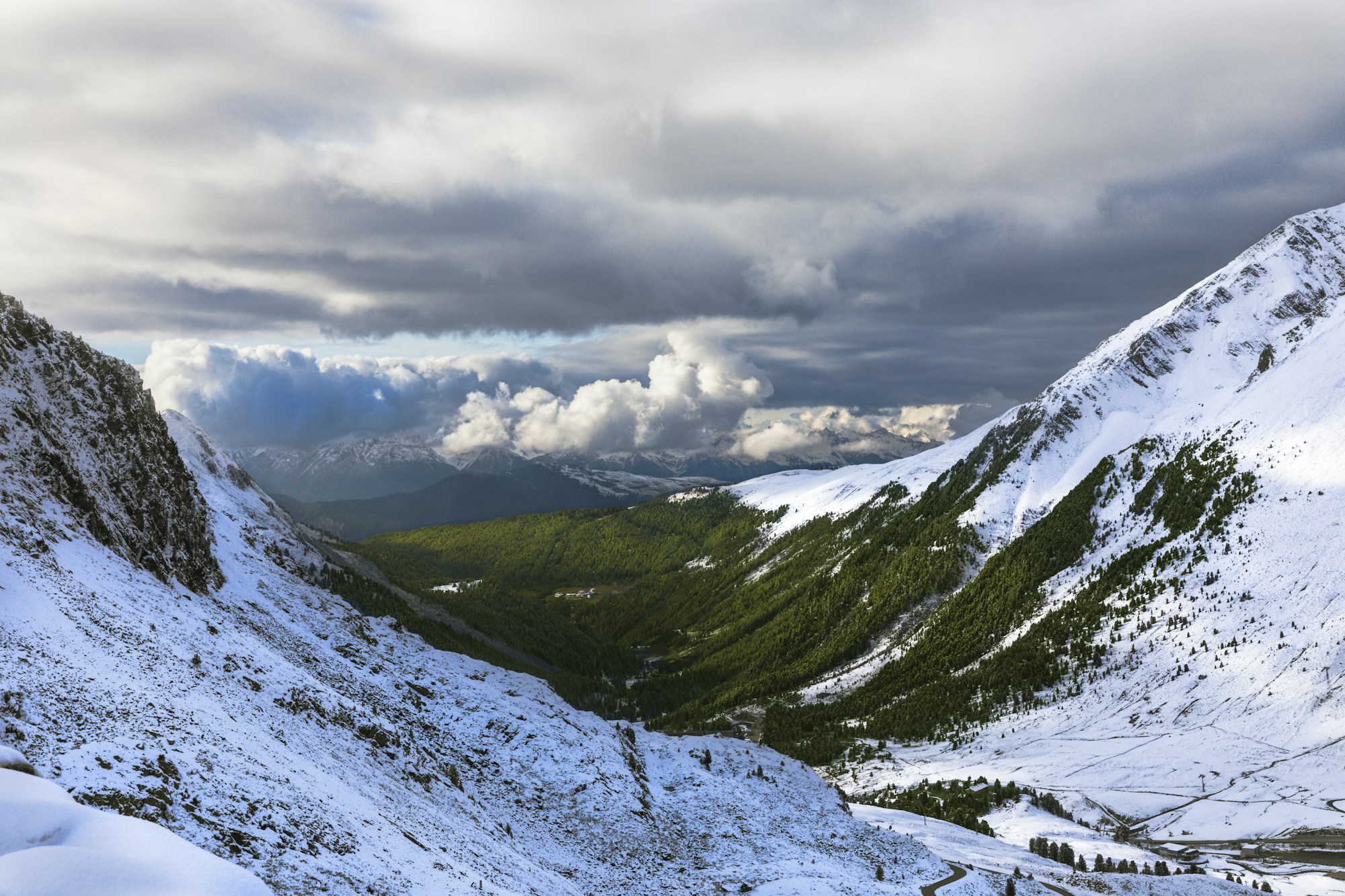 Vallée alpine enneigée sous un ciel d'hiver chargé, sommets couverts de neige et forêt de conifères