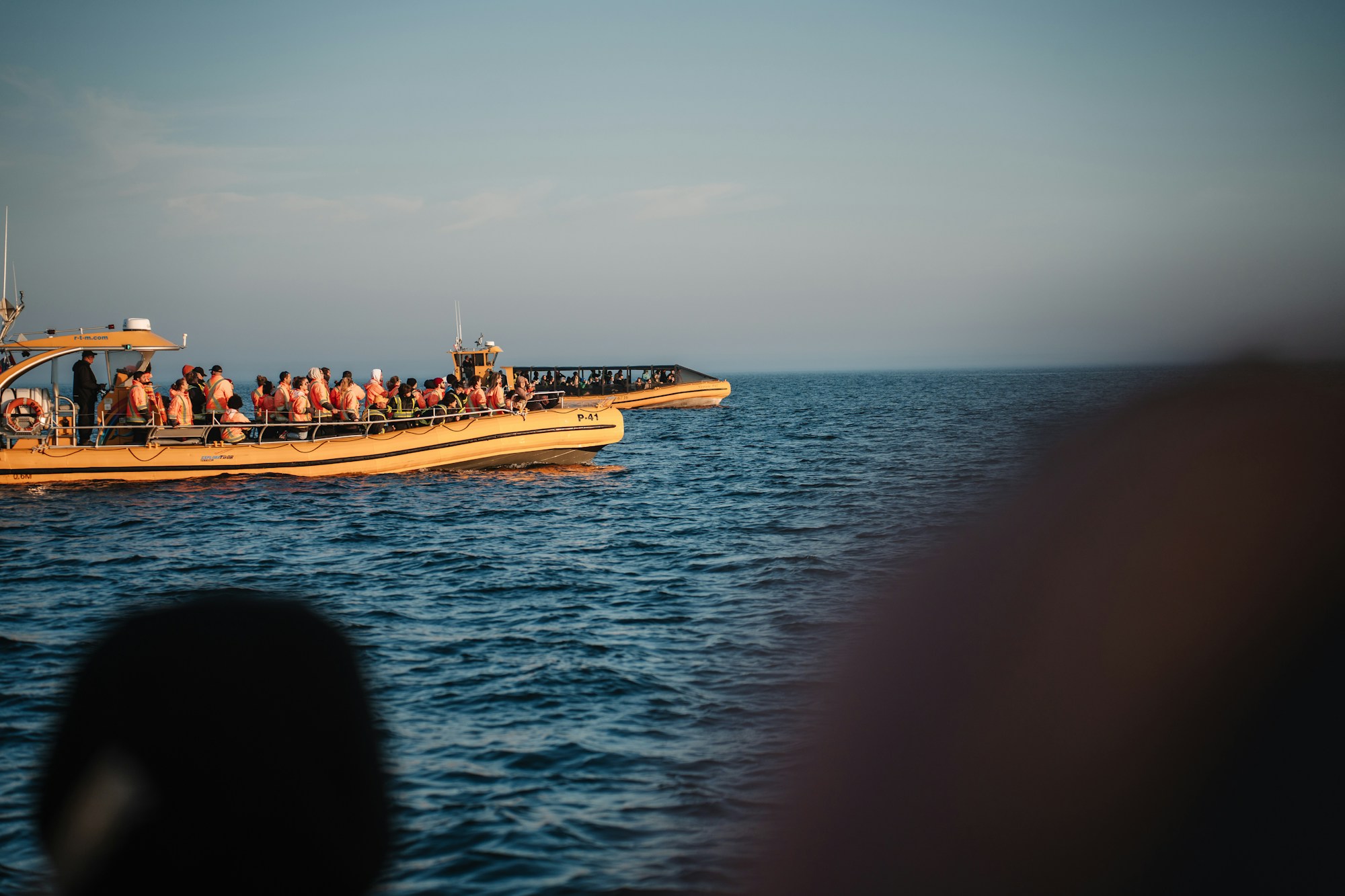 Deux bateaux pneumatiques jaunes transportant des passagers en gilets orange sur une mer bleue