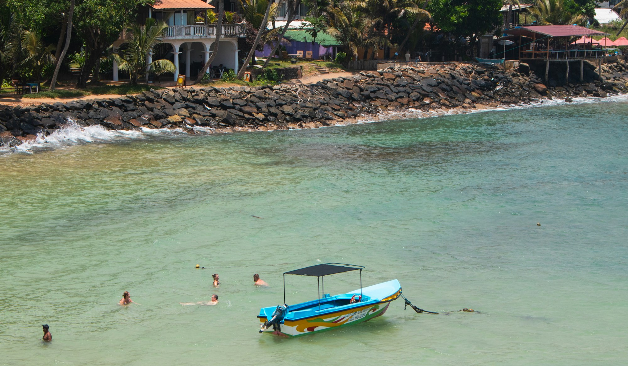 Petit bateau bleu sur la plage de Mirissa, avec des baigneurs dans l'eau turquoise