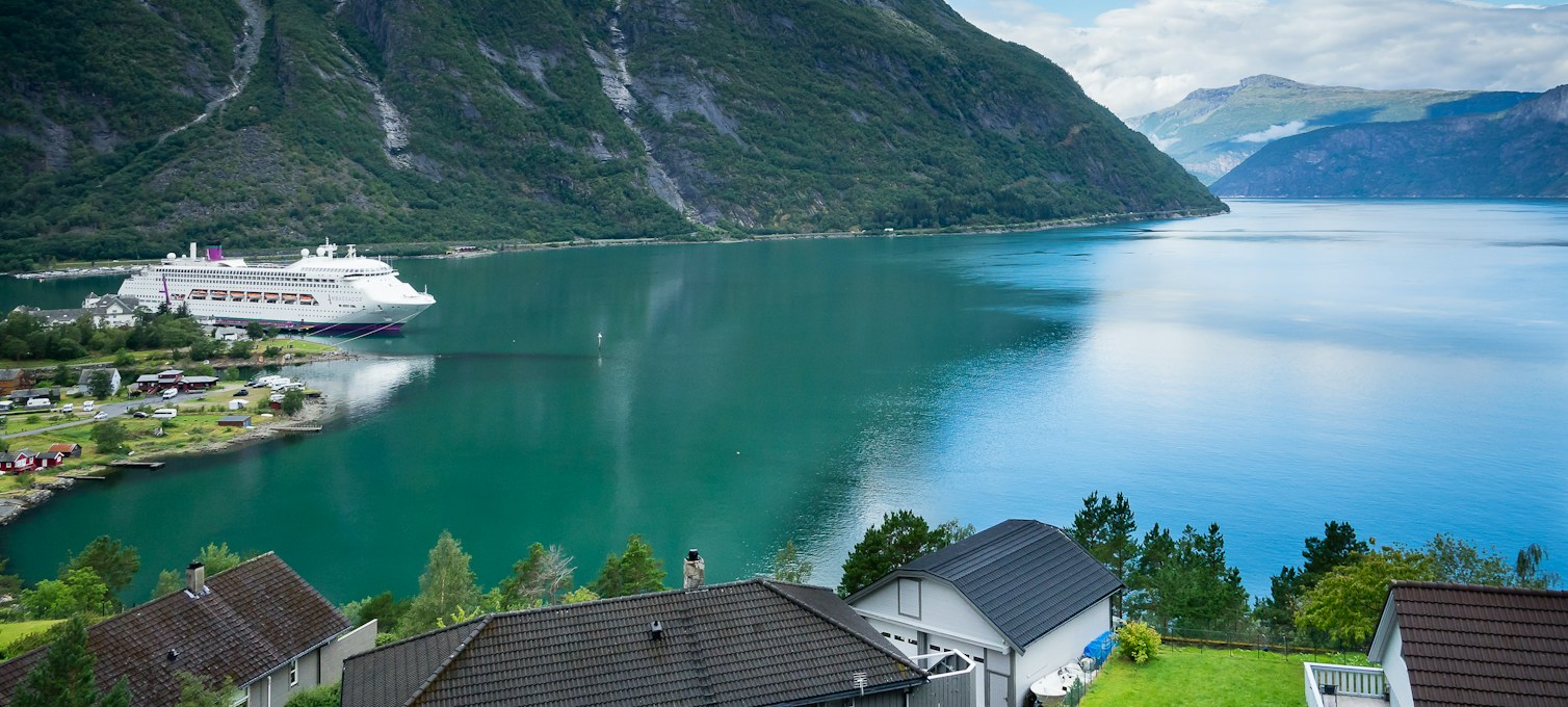 Cruise boat near a Norwegian fjord village, mountains in the background