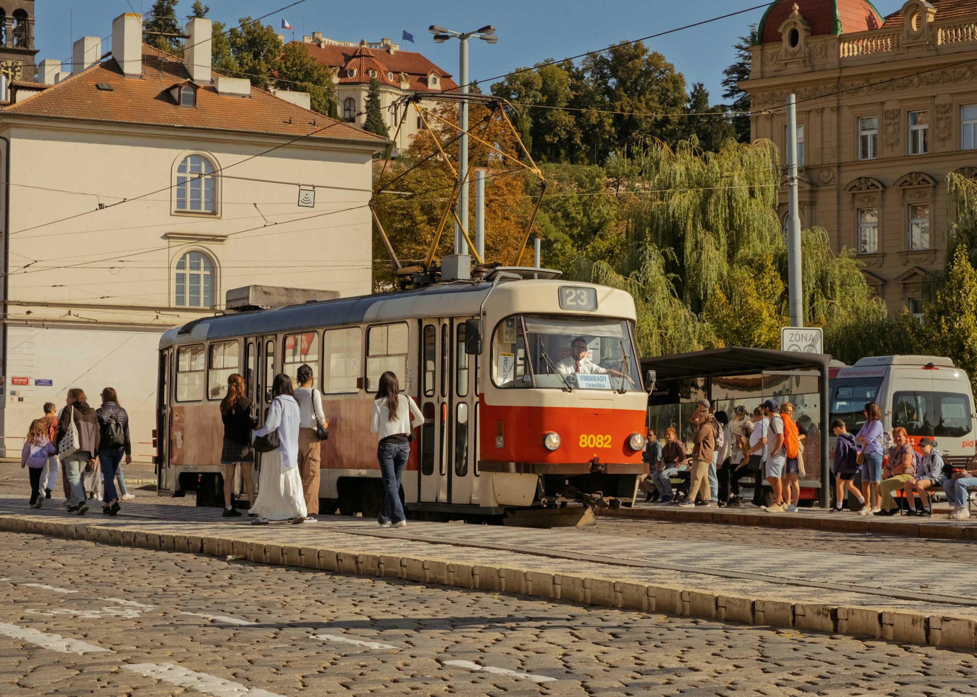Tramway et voyageurs à un arrêt pavé d'une rue de Prague